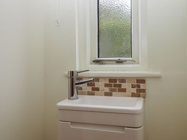 A small white sink with a chrome faucet below a frosted window and a wall section with brown and beige tiles at Binneford Barn Kennerleigh near Cheriton Fitzpaine