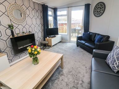 A living room with leather sofas a coffee table with flowers and a wall clock at Park View Lodge Arnside 7 South Lakeland Leisure Village near Carnforth