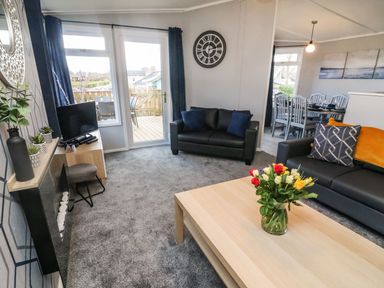 A living room with two black sofas a wooden coffee table with flowers and a wall clock at Park View Lodge Arnside 7 South Lakeland Leisure Village near Carnforth