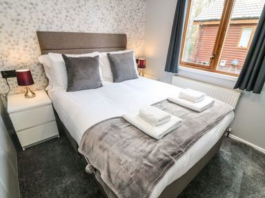 A bedroom with a double bed with white linens and gray pillows beside bedside tables with lamps at Park View Lodge Arnside 7 South Lakeland Leisure Village near Carnforth
