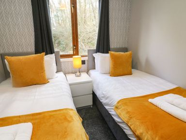 A bedroom with two single beds with yellow pillows and blankets a lamp on a nightstand between beds and a window with dark curtains at Park View Lodge Arnside 7 South Lakeland Leisure Village near Carnforth