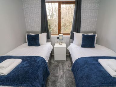 A bedroom with two single beds a nightstand lamp and a window at Park View Lodge Arnside 7 South Lakeland Leisure Village near Carnforth