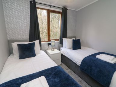 A bedroom with two single beds a nightstand and a window with curtains at Park View Lodge Arnside 7 in South Lakeland Leisure Village near Carnforth