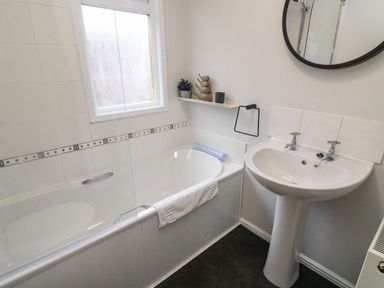 A bathroom with a bathtub next to a window and a pedestal sink with a round mirror above at Park View Lodge Arnside 7 South Lakeland Leisure Village near Carnforth
