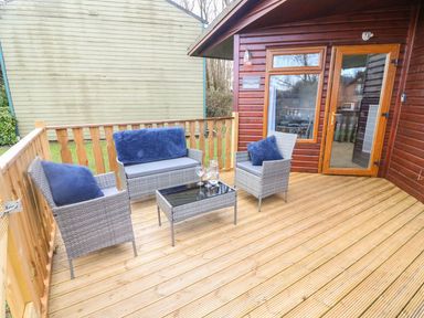An outdoor wooden deck with gray wicker furniture and blue cushions at Park View Lodge Arnside 7 South Lakeland Leisure Village near Carnforth
