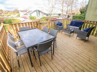 A wooden outdoor deck with dining table and chairs and seating area with cushions at Park View Lodge, Arnside 7 in South Lakeland Leisure Village near Carnforth