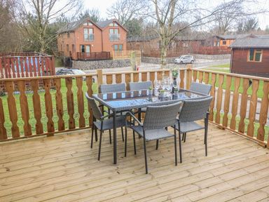 A wooden deck with a glass dining table and six chairs surrounded by a wooden railing at Park View Lodge Arnside 7 South Lakeland Leisure Village near Carnforth