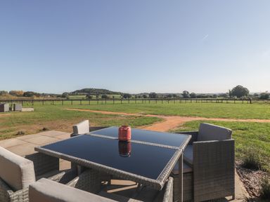 A patio table with chairs overlooking a fenced grassy field at Leadon View Oak in Upleadon near Newent