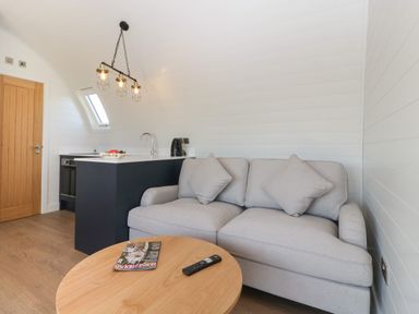 A small living area with a grey sofa, wooden round table, kitchen counter with sink and kettle at Leadon View Oak in Upleadon near Newent