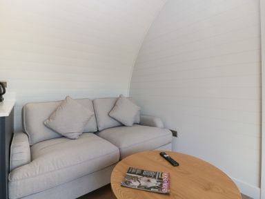A small living room with a grey couch a round wooden table with a magazine and remote at Leadon View Oak in Upleadon near Newent