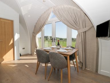 A dining area with a wooden table and four chairs near large glass doors with beige curtains at Leadon View Oak in Upleadon near Newent