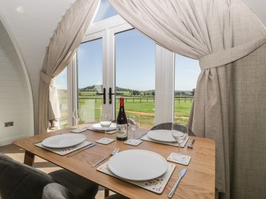 A dining table set for four with plates and wine glasses in front of glass doors showing green fields at Leadon View Oak in Upleadon near Newent