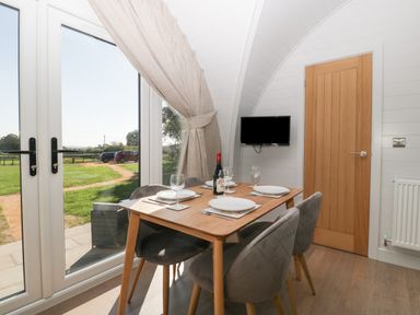 A dining area with a wooden table set for four and glass doors opening to a garden at Leadon View Oak in Upleadon near Newent