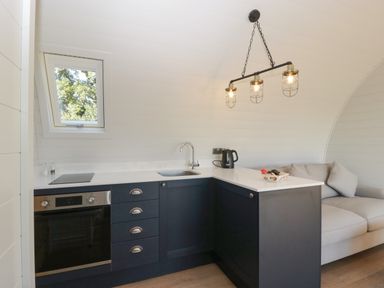 A kitchen corner with black cabinets a sink kettle and a window and a beige sofa at Leadon View Oak in Upleadon near Newent