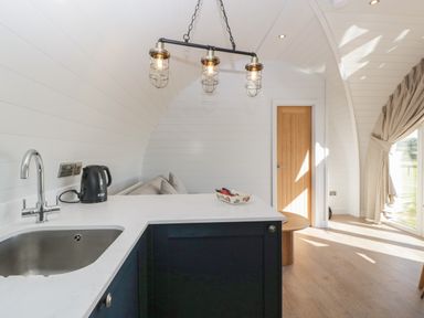 A kitchen area with a sink kettle and light fixtures next to a seating area with a table and window at Leadon View Oak in Upleadon near Newent