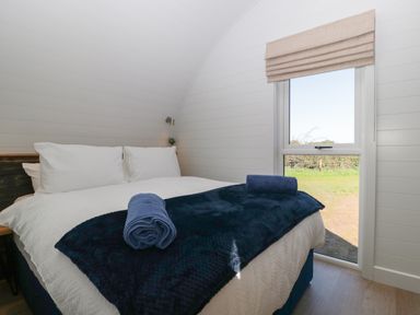 A bedroom with a bed covered in white linens and blue blankets next to a window at Leadon View Oak in Upleadon near Newent