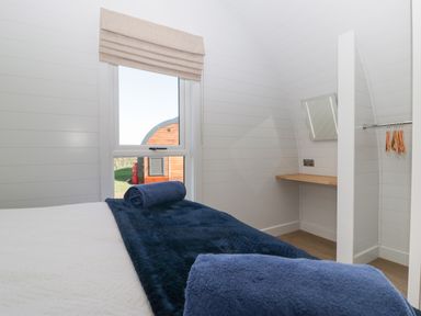 A bedroom with a bed covered by a blue blanket and rolled towel beside a window and a small wooden desk at Leadon View Oak in Upleadon near Newent
