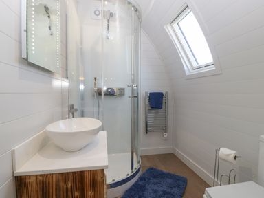 A bathroom with a curved glass shower enclosure a round vessel sink on a wooden vanity and a blue rug on the floor at Leadon View Oak in Upleadon near Newent