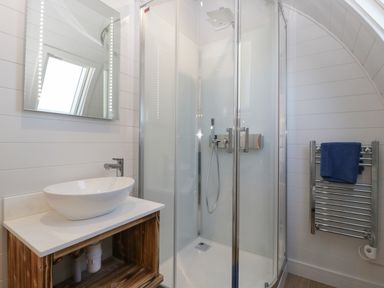 A bathroom with a glass shower enclosure a white basin on a wooden vanity and a towel rail with a blue towel at Leadon View Oak in Upleadon near Newent