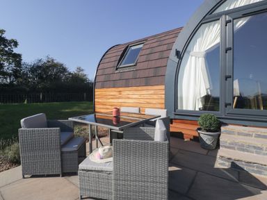 An outdoor seating area with a glass table and grey wicker chairs next to a curved wooden cabin at Leadon View Oak in Upleadon near Newent