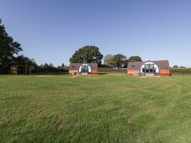 Two curved wooden cabins with glass fronts on a grassy field with trees in the background at Leadon View Oak in Upleadon near Newent