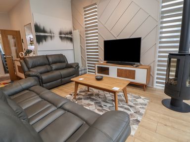 A living room with grey leather sofas a wooden coffee table a television on a stand and a wood stove at The Lodge @ Racecourse House in Babell near Holywell