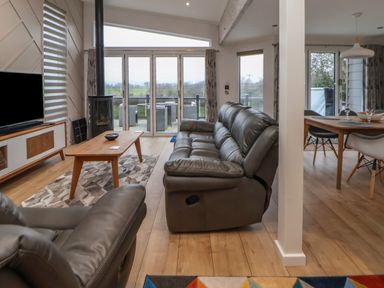 A living room with leather sofas a wooden coffee table a rug and a TV alongside a dining area with a table and chairs at The Lodge @ Racecourse House Babell near Holywell