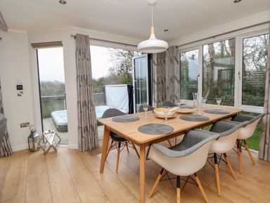 A dining room with a wooden table set with glasses and placemats next to large windows and glass doors at The Lodge @ Racecourse House Babell near Holywell