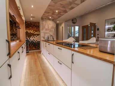A kitchen with wooden floors white cabinets a wooden countertop a stove a sink and two white chairs at The Lodge @ Racecourse House Babell near Holywell