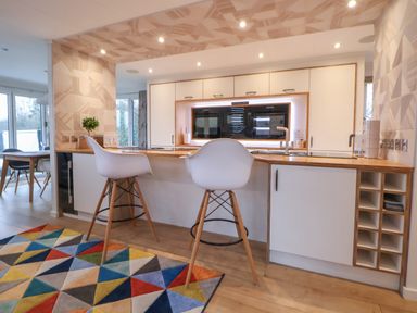 A kitchen with two white bar stools at a wooden countertop and a colorful geometric rug on the floor at The Lodge @ Racecourse House Babell near Holywell