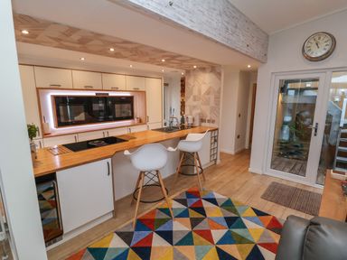 A kitchen with a wooden countertop and two white bar stools and a colorful geometric rug on the floor at The Lodge @ Racecourse House Babell near Holywell