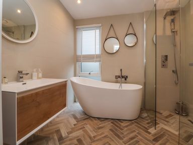 A bathroom with a freestanding bathtub two round mirrors a sink with a wooden cabinet and a glass shower enclosure at The Lodge @ Racecourse House in Babell near Holywell