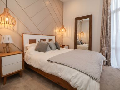 A bedroom with a bed and pillows bedside tables with lamps a large mirror and curtains at The Lodge @ Racecourse House Babell near Holywell