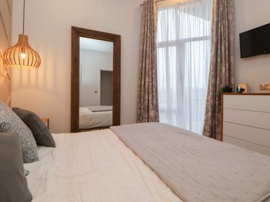 A bedroom with a bed pillows a blanket a wooden-framed mirror curtains a hanging light and a dresser with a plant at The Lodge @ Racecourse House Babell near Holywell