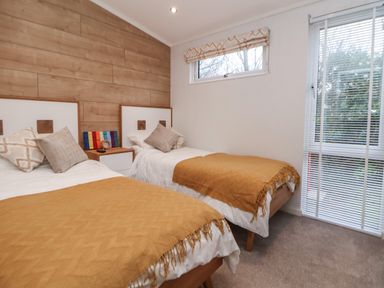 A bedroom with two single beds with mustard blankets and pillows a wooden accent wall and windows with blinds at The Lodge @ Racecourse House in Babell near Holywell