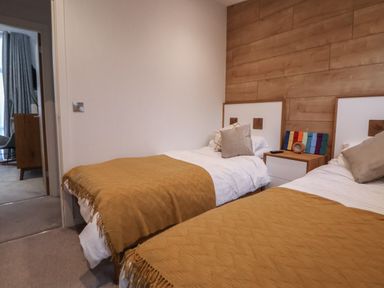 A bedroom with two single beds with mustard blankets and pillows and a wooden nightstand between the beds at The Lodge @ Racecourse House in Babell near Holywell
