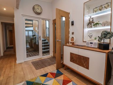 An entryway with wooden floor a glass door leading outside a wooden cabinet with decorative items a clock on the wall at The Lodge @ Racecourse House Babell near Holywell