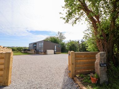 A lodge with a gravel driveway and wooden fence at The Lodge @ Racecourse House in Babell near Holywell
