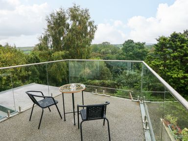 A balcony with two black chairs and a small round table overlooking green trees at Rushfield in St Dogmaels North Pembrokeshire