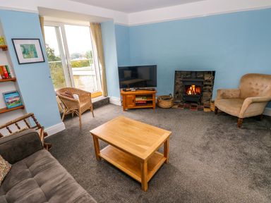 A living room with a wooden coffee table a TV on a wooden stand a fireplace and seating at Rushfield in St Dogmaels North Pembrokeshire