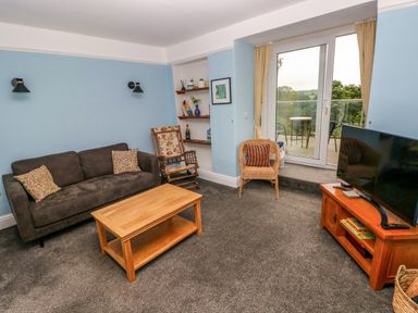 A living room with a sofa coffee table rocking chair wicker chair television and a balcony door at Rushfield in St Dogmaels North Pembrokeshire