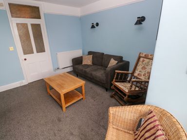 A living room with a grey sofa wooden coffee table rocking chair and wicker chair at Rushfield in St Dogmaels North Pembrokeshire