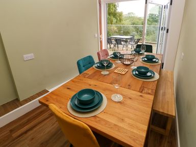 A dining table set with plates bowls and glasses in a room with an open glass door leading to an outdoor patio at Rushfield in St Dogmaels North Pembrokeshire