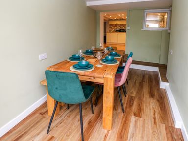 A dining room with a wooden table set with plates and glasses and colored chairs at Rushfield in St Dogmaels North Pembrokeshire