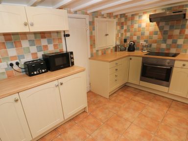 A kitchen with cream cabinets black toaster and microwave oven and tiled backsplash at Rushfield in St Dogmaels North Pembrokeshire