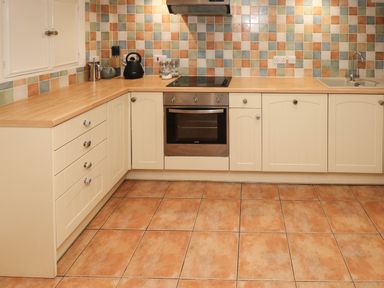 A kitchen with cream cabinets a black kettle a stove oven and a sink at Rushfield St Dogmaels North Pembrokeshire