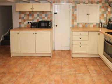 A kitchen with tiled floor and multi colored tiled backsplash with cream cabinets a microwave toaster and kettle on countertops at Rushfield in St Dogmaels North Pembrokeshire