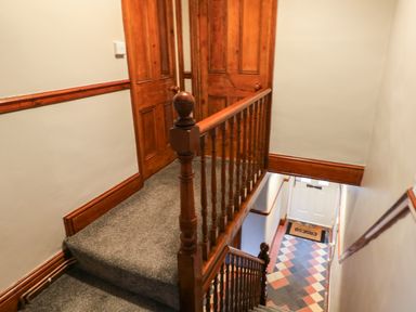 A staircase with wooden banisters leading down to a door with a tiled floor and two wooden doors at the top of the stairs at Rushfield in St Dogmaels North Pembrokeshire