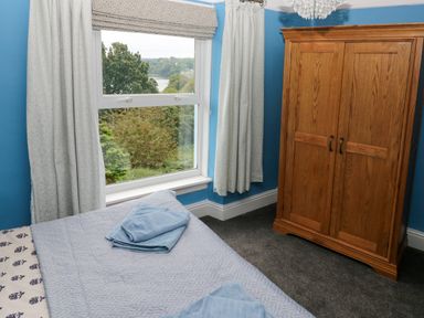 A bedroom with a bed and folded towels next to a window and a wooden wardrobe at Rushfield in St Dogmaels North Pembrokeshire