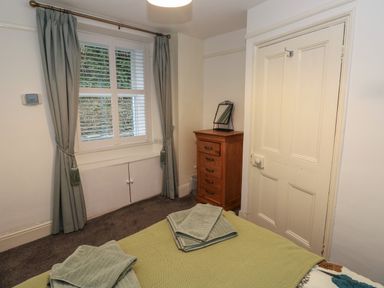 A bedroom with a bed folded towels a wooden chest of drawers and a window with curtains at Rushfield in St Dogmaels North Pembrokeshire